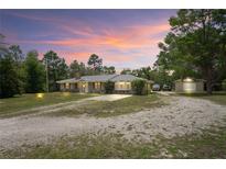 Charming single-story home with a spacious driveway, detached garage and metal roof surrounded by lush landscaping at 13345 Convent Garden Rd, Brooksville, FL 34613