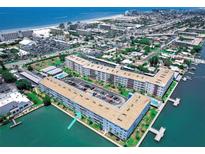 Aerial view of a waterfront condo complex with boat docks, pool, and parking, near the beach in a coastal neighborhood at 5555 Gulf Blvd # 315, St Pete Beach, FL 33706