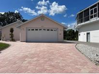A well-maintained pink house with a two-car garage and a patterned brick driveway under a blue sky at 20971 Negril Ct, Lutz, FL 33558
