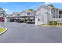 View of covered parking spaces at The Hillside community with grey condo buildings on a bright, sunny day at 12141 Spartan Way # 102, Hudson, FL 34667