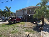 Beige two-story house with a garage, wooden stairs to the porch, palm trees, and a red jeep in the yard at 5420 Bay Blvd, Port Richey, FL 34668