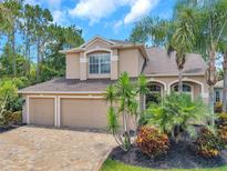 Inviting two-story home with a three-car garage, brick paver driveway, and mature tropical landscaping at 10925 Oyster Bay Cir, New Port Richey, FL 34654