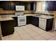 Compact kitchen featuring dark cabinets, white appliances, and tile flooring at 6524 Ouida Way, Las Vegas, NV 89108