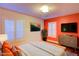 Virtually staged bedroom with an orange accent wall, white bedding, and plantation shutters at 664 California Ave, Boulder City, NV 89005