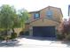 Two-story house with tan exterior, dark garage door, and landscaping at 647 Wounded Star Ave, Las Vegas, NV 89178