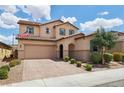 Two-story home featuring a tile roof, brick driveway, desert landscaping, and a front yard tree at 2130 Danzinger Pl, Henderson, NV 89044