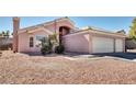 Exterior view of a light pink house with a two-car garage and rock landscaping at 1187 Merlin Ct, Henderson, NV 89002