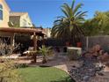 Landscaped backyard featuring a pergola, palm trees, and rock garden at 853 Teal Ave, Las Vegas, NV 89123