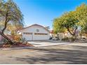 White house with a three-car garage and mature trees, showcasing curb appeal at 1265 Del Lilly Ln, Las Vegas, NV 89123