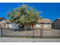 Tan house with a white garage door, black metal fence, and large green tree in front at 213 Samantha St, Las Vegas, NV 89110