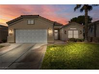 Tan one-story house with white garage door and landscaped yard at dusk at 565 Fairways Dr, Mesquite, NV 89027