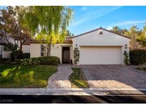 Single-story home with a white exterior, landscaped yard, and two-car garage at 11775 Woodbrook Ct, Las Vegas, NV 89141